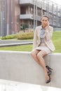 Full length of young businesswoman using mobile phone while sitting on wall against office building Royalty Free Stock Photo