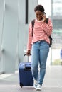 Full length young female traveler walking in airport terminal with suitcase and mobile phone Royalty Free Stock Photo