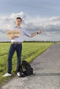 Full length of young man hitching while holding anywhere sign on countryside