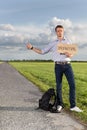 Full length of young man hitching while holding anywhere sign on countryside