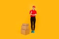 Full length young woman courier standing near cardboard boxes on yellow background Royalty Free Stock Photo