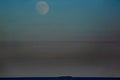 Almost Full Moon above Haze -filled sky and Ship on Horizon