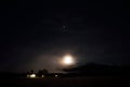 Full moon on autumn night sky over mountain, field and lit houses Royalty Free Stock Photo