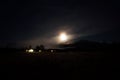 Full moon on autumn night sky over mountain, field and lit houses Royalty Free Stock Photo