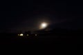 Full moon on autumn night sky over mountain, field and lit houses Royalty Free Stock Photo