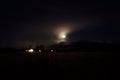 Full moon on autumn night sky over mountain, field and lit houses Royalty Free Stock Photo