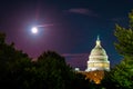 Full moon behind United States capitol building illuminates it marble dome at night with trees silhouetted in foreground Royalty Free Stock Photo