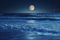 A full moon brightens the night sky and casts a glowing light over the crashing waves in the ocean, A midnight scene of tranquil Royalty Free Stock Photo