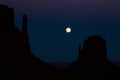 Full moon in dark sky above silhouette of desert towers in Souther Utah/Arizona Monument Valley