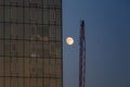 A full moon next to a Manhattan skyscraper building and a crane