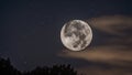 full moon in the night sky A bright full moon in a dark night sky, with a few stars and clouds visible.