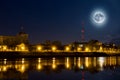 Full moon over the city. Night landscape. Lantern lights are reflected in water. Supermoon.