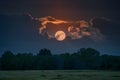 Full moon peeks through dark clouds, casting an eerie glow