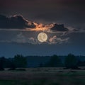 Full moon peeks through dark clouds, casting an eerie glow