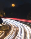 Full moon rising above a curving highway. Light trails from cars speeding by Royalty Free Stock Photo