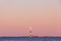 Full moon rising through the Belt of Venus behind a tall stone lighthouse at sunset.