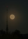 Full moon rising into the night sky with a radio antenna and transmission tower with a red signal light Royalty Free Stock Photo