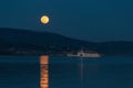 Full moon rising over some hills on a lake, perfectly reflecting on water near an incoming boat Royalty Free Stock Photo
