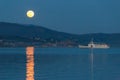 Full moon rising over some hills on Trasimeno lake, perfectly reflecting on water with a ferry nearby Royalty Free Stock Photo