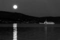 Full moon rising over some hills on Trasimeno lake, perfectly reflecting on water with a ferry nearby Royalty Free Stock Photo