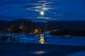 Full moon setting over the mountains at dawn with boats in the bay