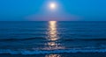 Full moon shining brightly over a tranquil ocean, casting a long, silvery reflection on the Royalty Free Stock Photo
