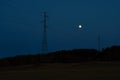 Full moon at twilight with silhouettes of electrycity towers and forest.