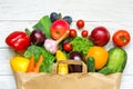 Full paper bag of different fruits and vegetables on a white wooden background