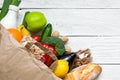 Full paper bag of different healthy vegetarian food on white wooden background. fruits, vegetables, nuts, bread and milk