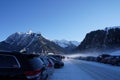 Full parking lot with cars in cross country skiing resort in Switzerland surrounded by snow capped mountains.