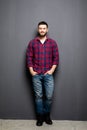 Full Portrait of handsome young man in casual shirt with hands in pockets and smiling while standing against grey background Royalty Free Stock Photo