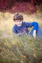 Smiling seven year old boy portrait sitting in field in Autumn