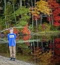 Full portrait of a smiling nine year old boy outside by a lake with colorful fall trees