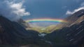 Full rainbow over a mountain valley. Atmospheric alpine landscape with snowy mountains with rainbow in rainy and sunny weather Royalty Free Stock Photo