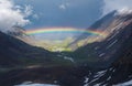 Full rainbow over a mountain valley. Atmospheric alpine landscape with snowy mountains with rainbow in rainy and sunny weather Royalty Free Stock Photo