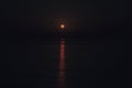 The Full Red Moon Shines Brightly in the Sky on a Dark Night Over the Calm Sea. Beautiful Moon Path on the Water Royalty Free Stock Photo