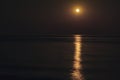 The Full Red Moon Shines Brightly in the Sky on a Dark Night Over the Calm Sea. Beautiful Moon Path on the Water Royalty Free Stock Photo