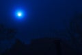 Full shiny moon on the dark clear blue sky over the lonely roof and trees