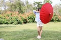 Full shot happy and cute child girl holding red umbrella in park with green trees and flowers background Royalty Free Stock Photo