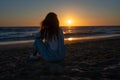woman in a denim jumpsuit sitting on the sand of a beach watching the sun set over the sea Royalty Free Stock Photo