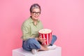 Full size body photo of cheerful business lady sit box cube holding bucket pop corn snacks watch films isolated on pink