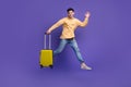 Full size photo of attractive young man jumping run wave hand suitcase dressed stylish yellow clothes isolated on purple Royalty Free Stock Photo