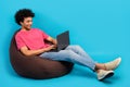 Full size photo of attractive young man sitting brown beanbag netbook manager wear trendy pink outfit isolated on blue Royalty Free Stock Photo