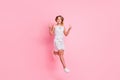 Full size photo of cute blond girl jumping show v-sign wear white dress sneakers isolated on pastel pink color Royalty Free Stock Photo