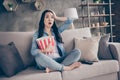 Full size photo of frightened girl sit divan legs crossed folded barefoot watch horror movie hold big pop corn box