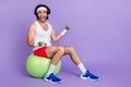 Full size photo of funky happy young man hold dumbbells sit green fit ball smile isolated on purple color background Royalty Free Stock Photo