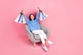 Full size photo of funny woman wear knit pullover trousers raising shopping bags sit on armchair on pink color