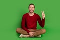 Full size photo good mood nice guy wear red shirt brown trousers sit on floor showing v-sign symbol isolated on green Royalty Free Stock Photo