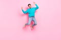 Full size photo of handsome young guy jumping raise hands excited have fun wear trendy blue garment isolated on pink