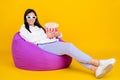 Full size photo of millennial lady sit bean chair hold pop corn basket isolated over shine yellow color background